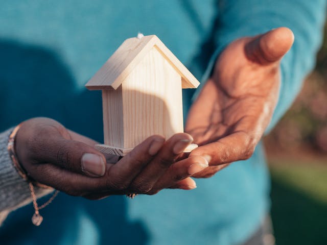 person holding a wooden home figurine